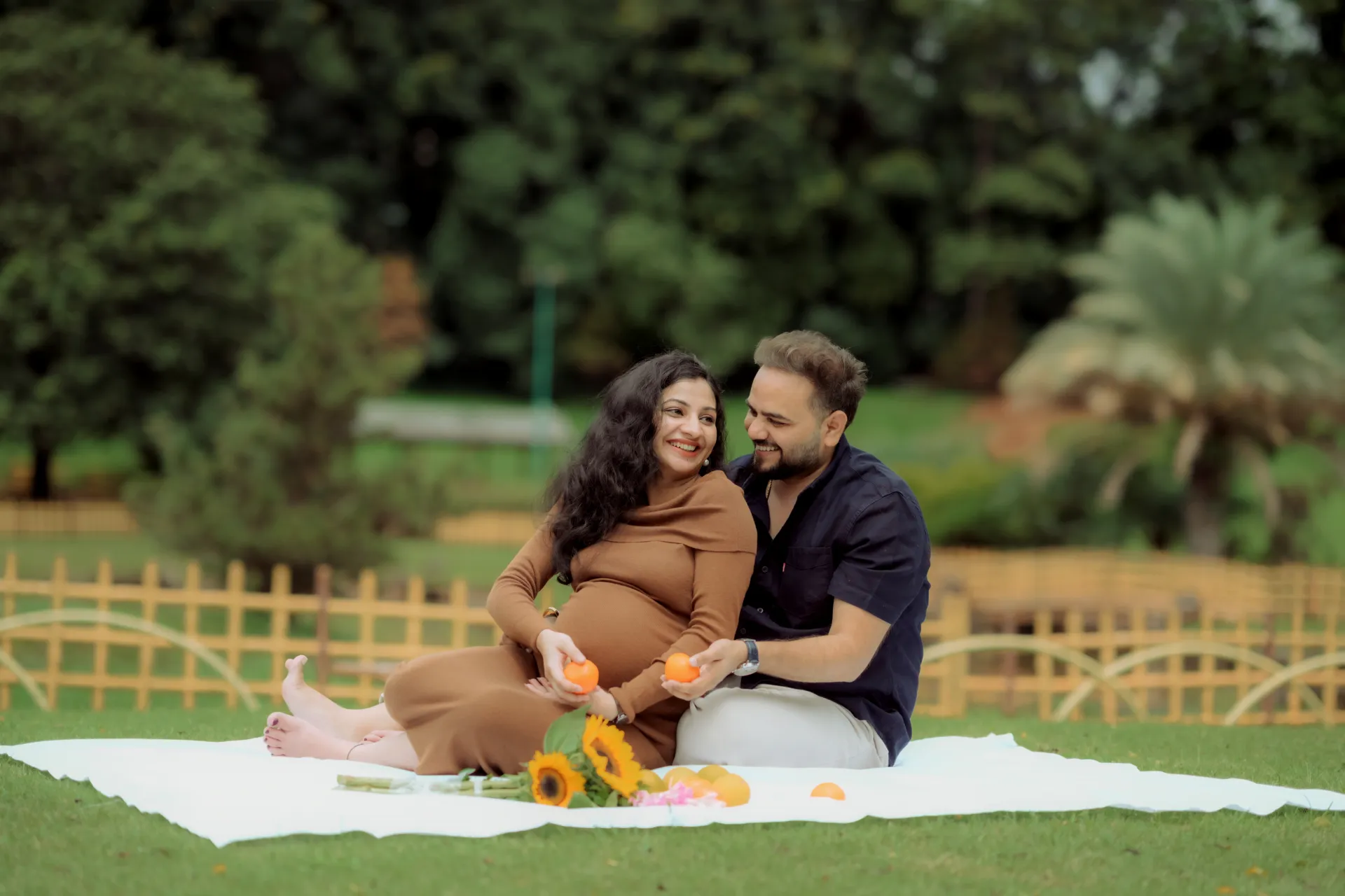 Maternity photoshoot in Pune - expecting couple on a picnic blanket with sunflowers and oranges